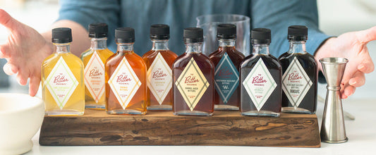 A line up of all The Bitter Housewife bitters flavors on a thick wooden tray